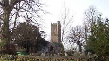 A church with a tall tower, surrounded by trees and a stone wall.