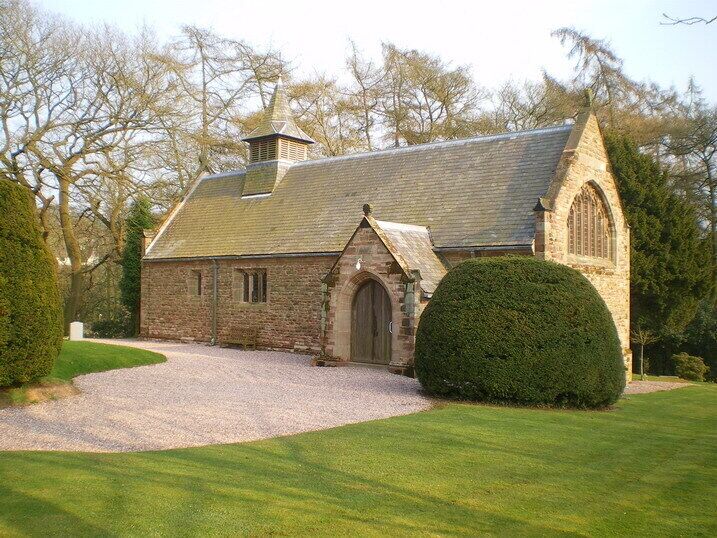 A stone church with a pointed arch entrance, a bell tower, and a gravel driveway.