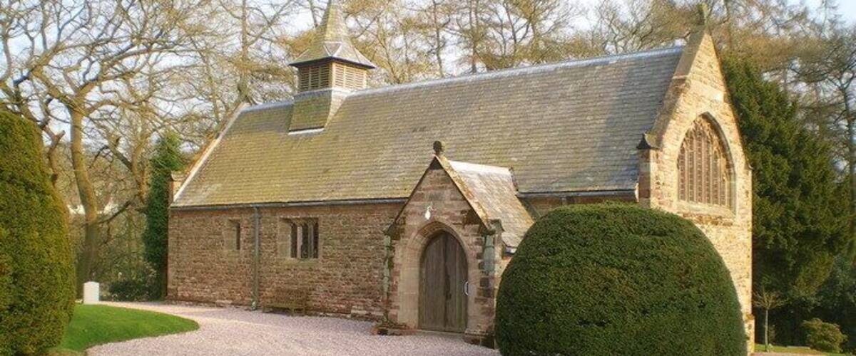 A stone church with a pointed arch entrance, a bell tower, and a gravel driveway.
