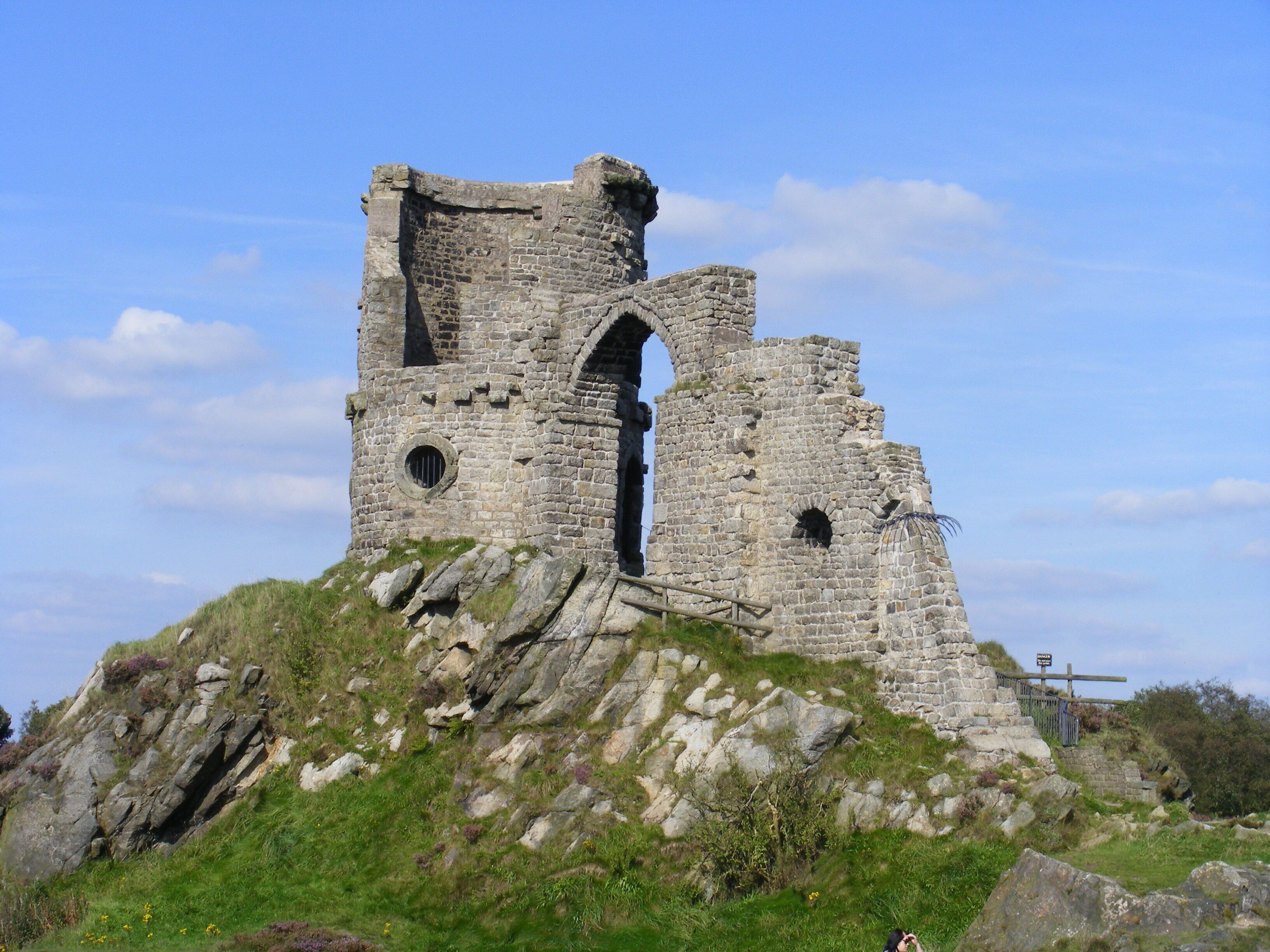 A medieval stone tower with arched windows and a staircase leading up to it, surrounded by grassy terrain and a clear sky.