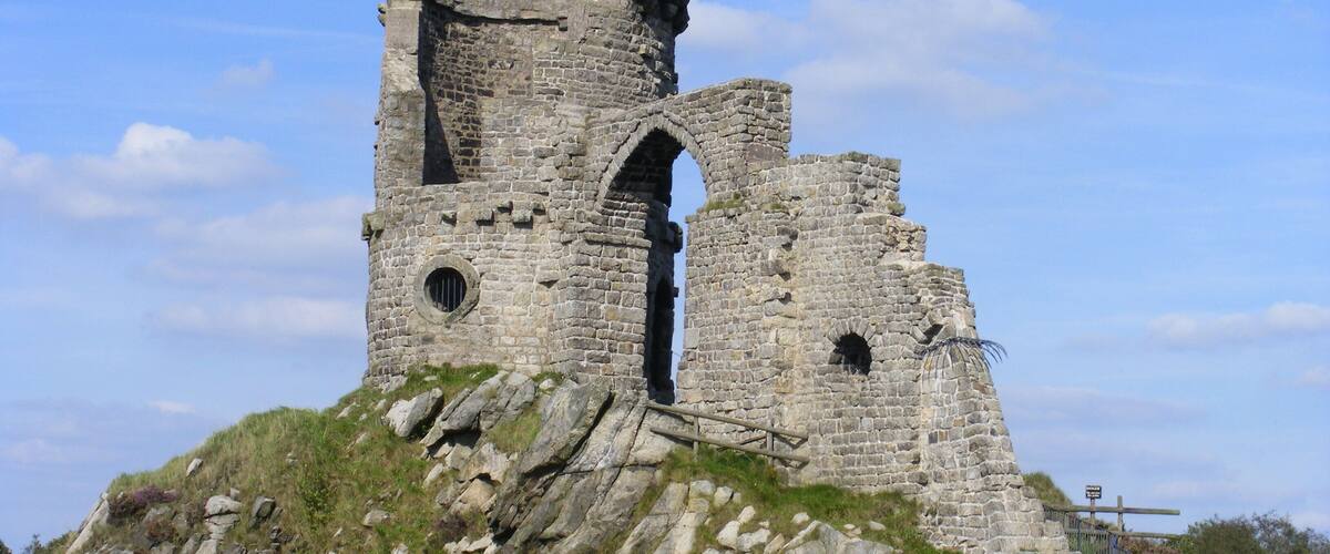 A medieval stone tower with arched windows and a staircase leading up to it, surrounded by grassy terrain and a clear sky.