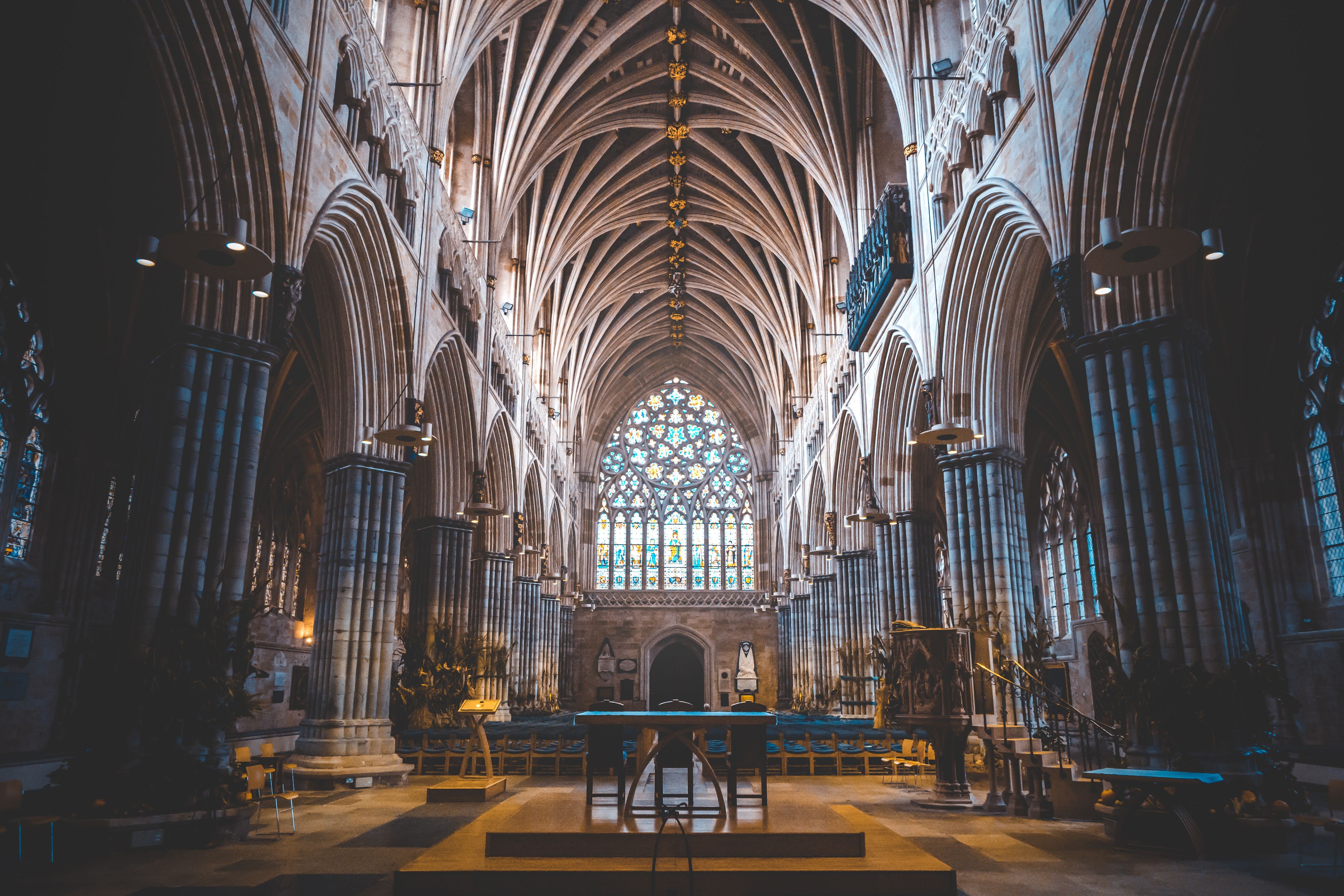 A cathedral interior with high vaulted ceilings, large stained glass windows, and rows of pews.