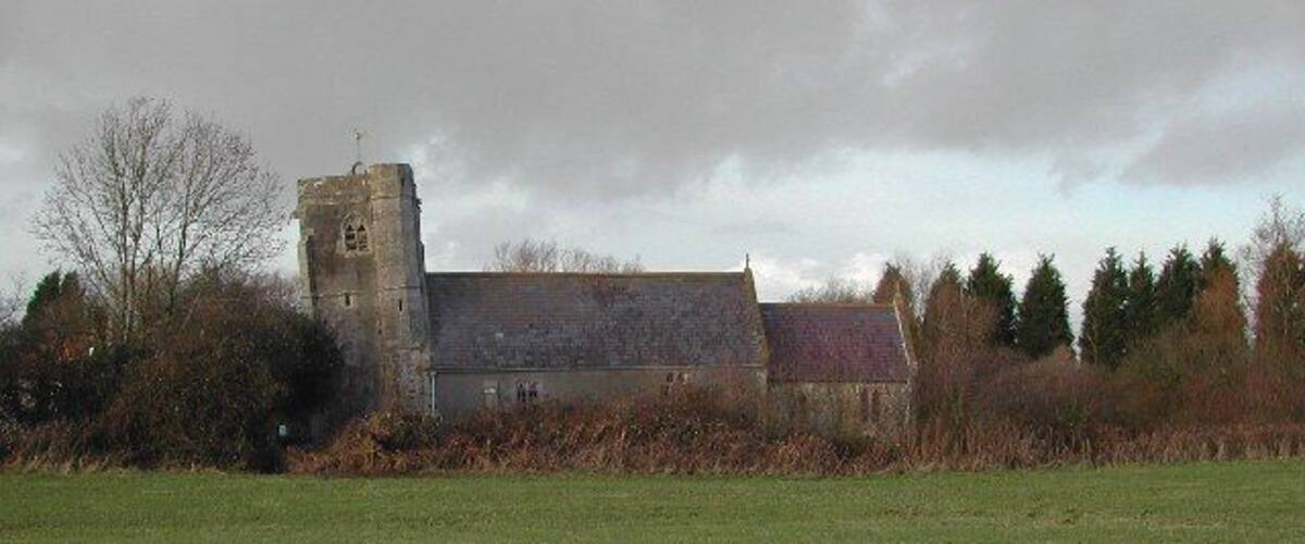 A church with a bell tower and a stone building surrounded by a grassy field and trees.