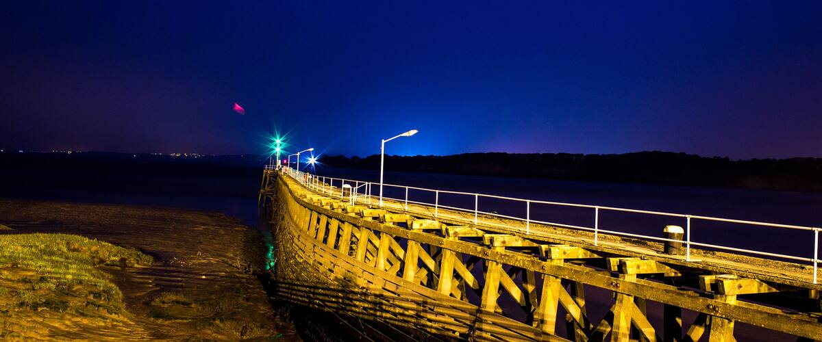 A wooden pier extending into a body of water at night, illuminated by streetlights.