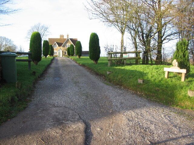 A gravel driveway leading to a house with a well-maintained lawn and trimmed hedges.