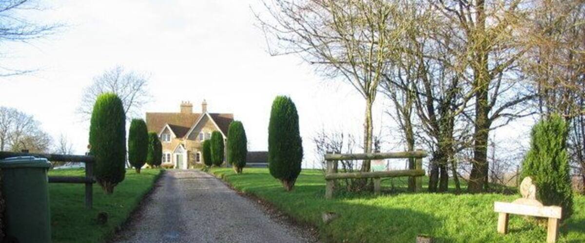 A gravel driveway leading to a house with a well-maintained lawn and trimmed hedges.