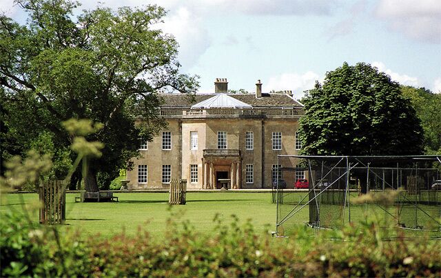 A large stone building with a central entrance, surrounded by a well-maintained lawn and trees.