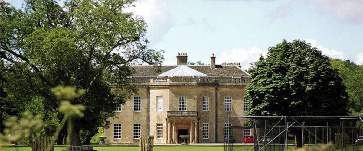 A large stone building with a central entrance, surrounded by a well-maintained lawn and trees.