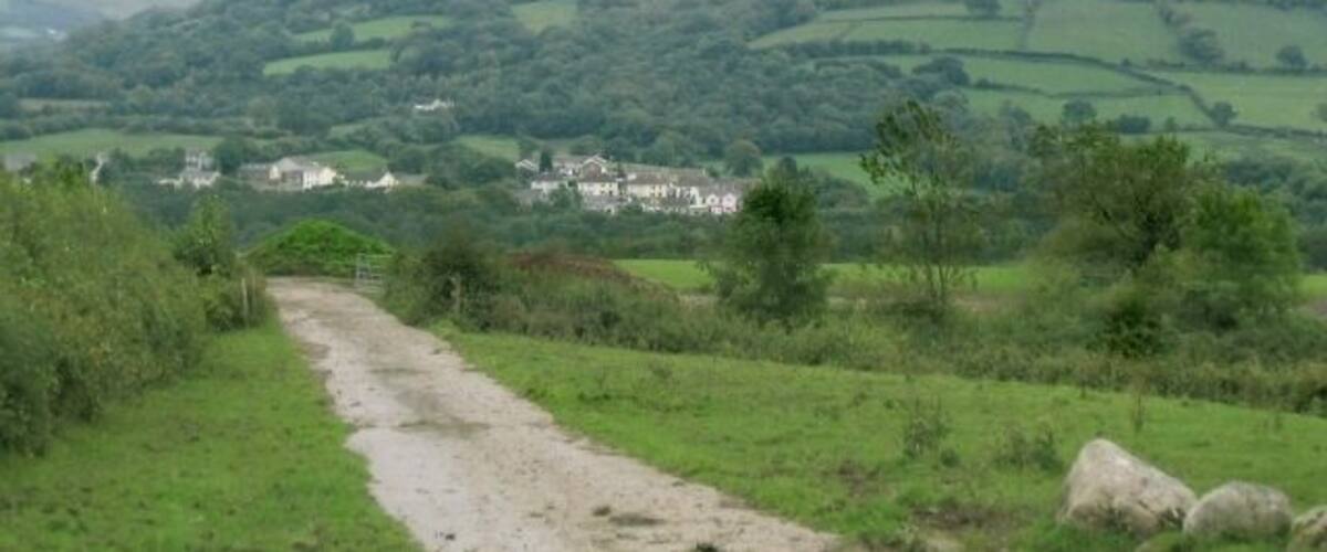 A rural landscape with rolling hills, a dirt path, and a small village in the distance.