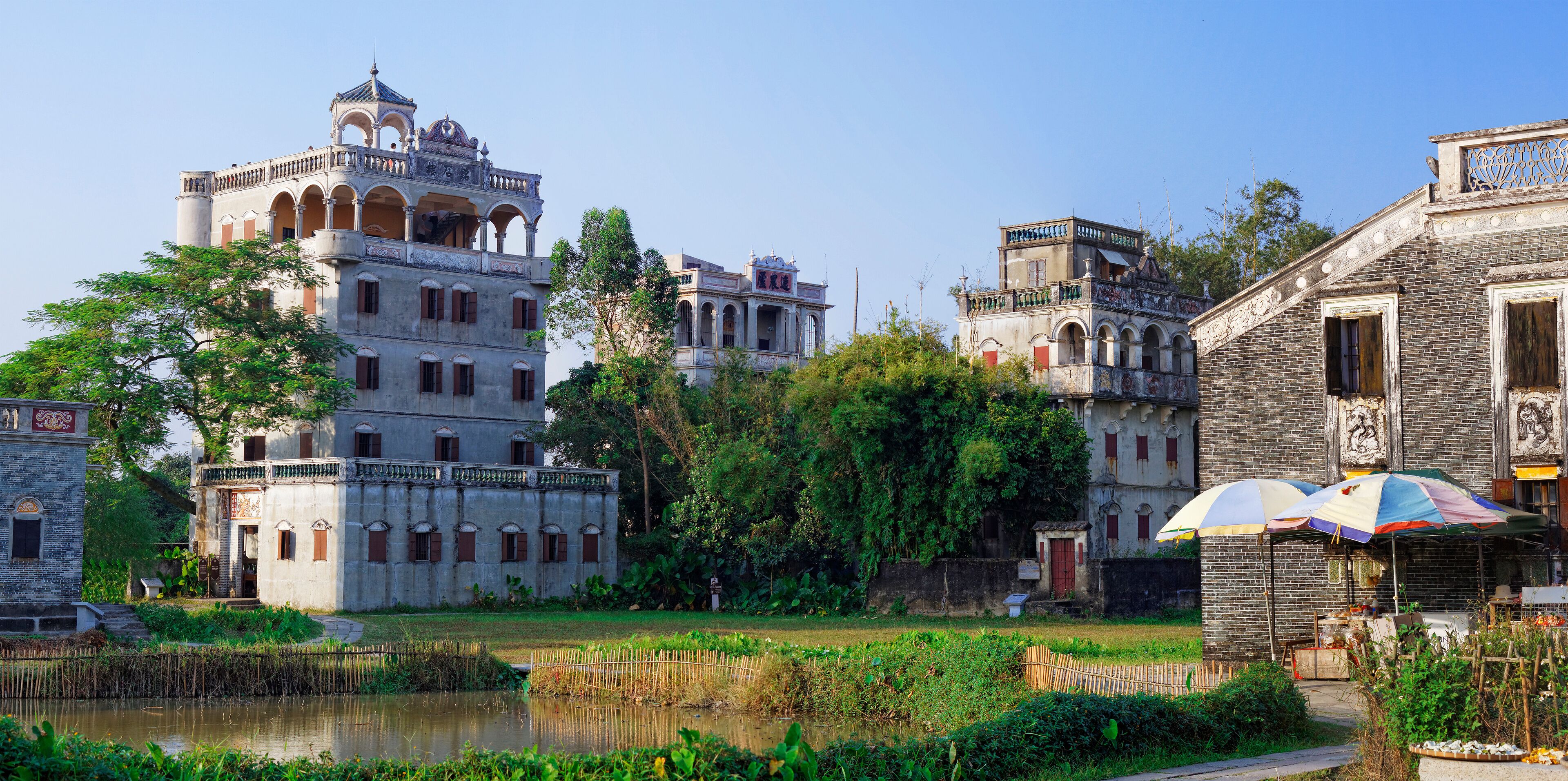 A historic building with multiple levels and a tower, surrounded by lush greenery and a small pond.