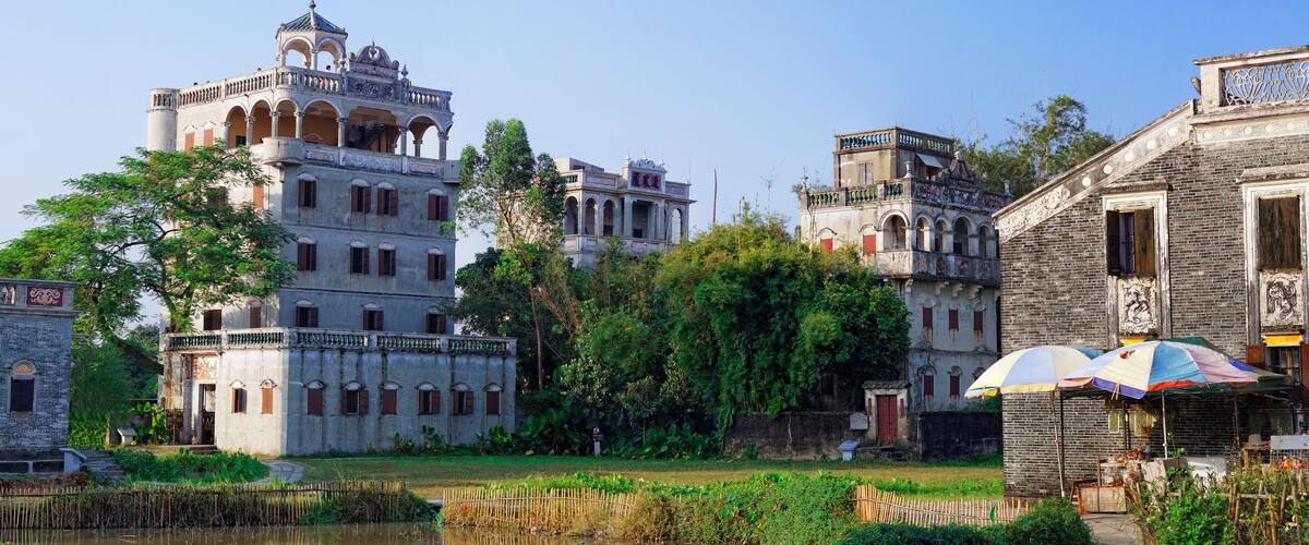 A historic building with multiple levels and a tower, surrounded by lush greenery and a small pond.