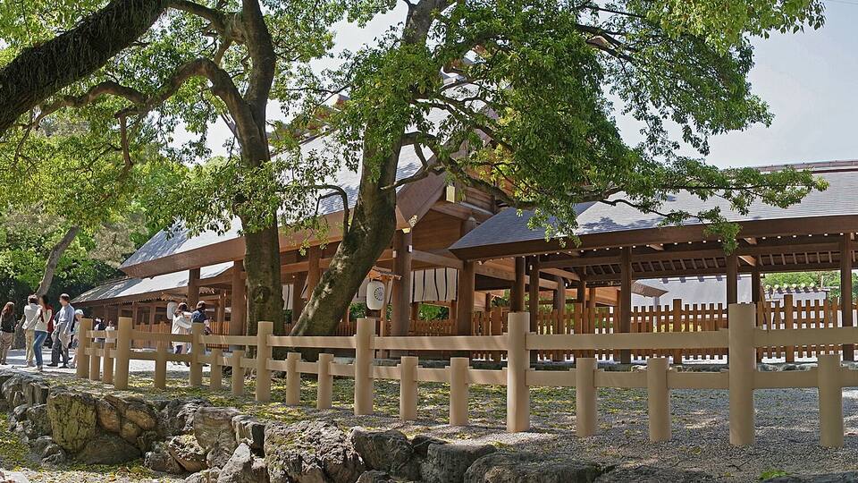 Ein traditionelles japanisches Pavillon mit geschwungener Dachform, umgeben von Bäumen und Kieswegen.