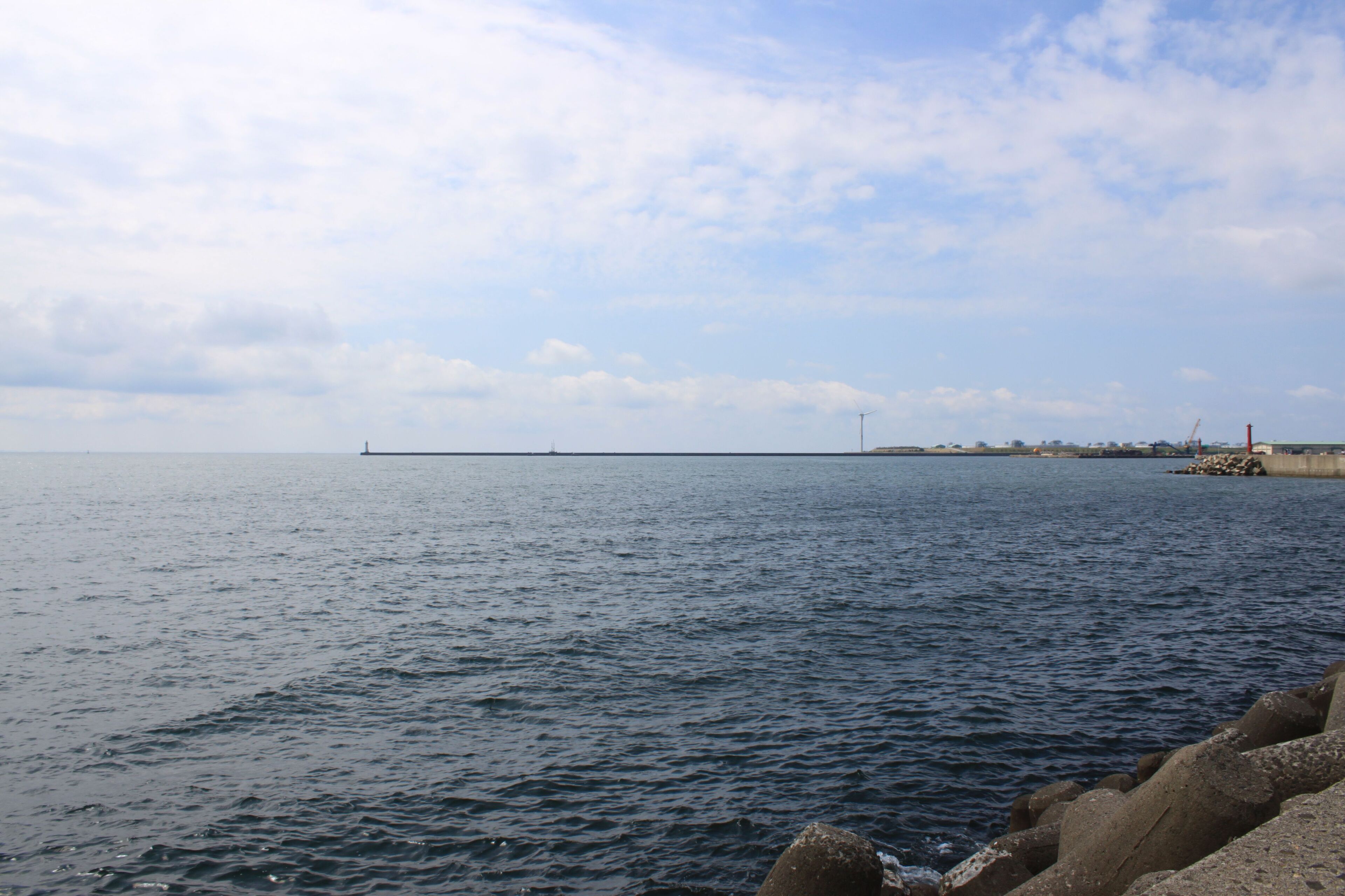 A calm sea with a rocky breakwater and a distant pier.