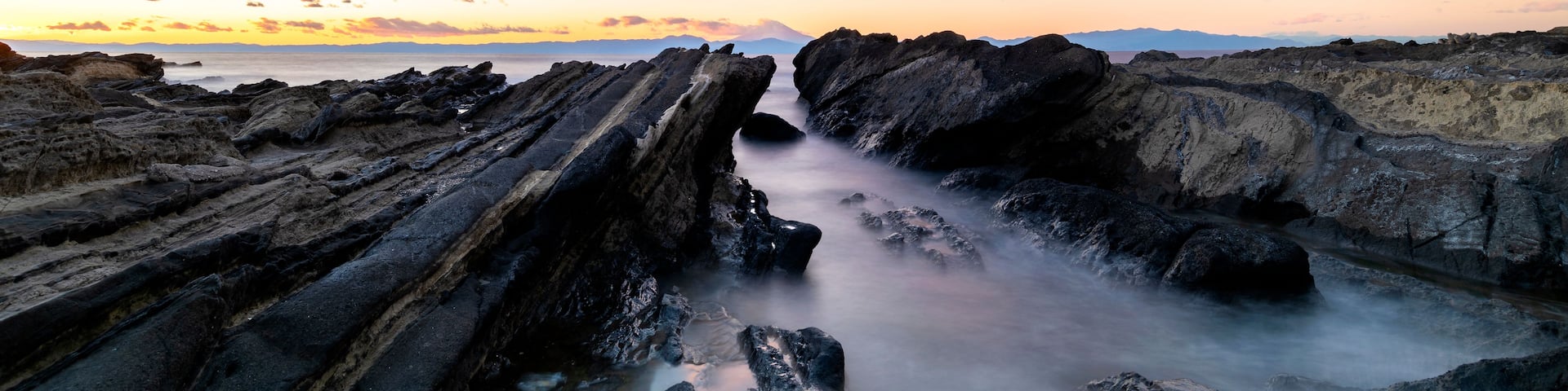 A rocky landscape with a river flowing through it, under a colorful sky with clouds.