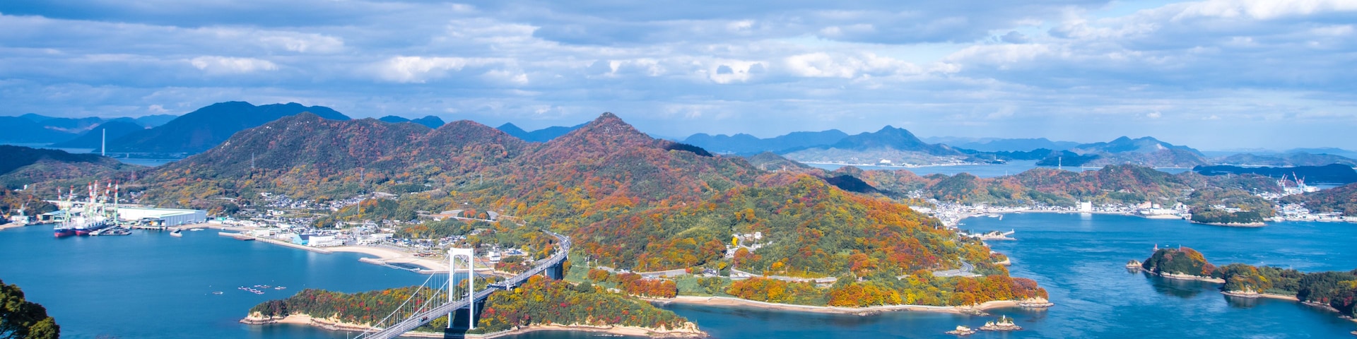 Un paisaje costero con un puente colgante, un ferry y terreno montañoso.