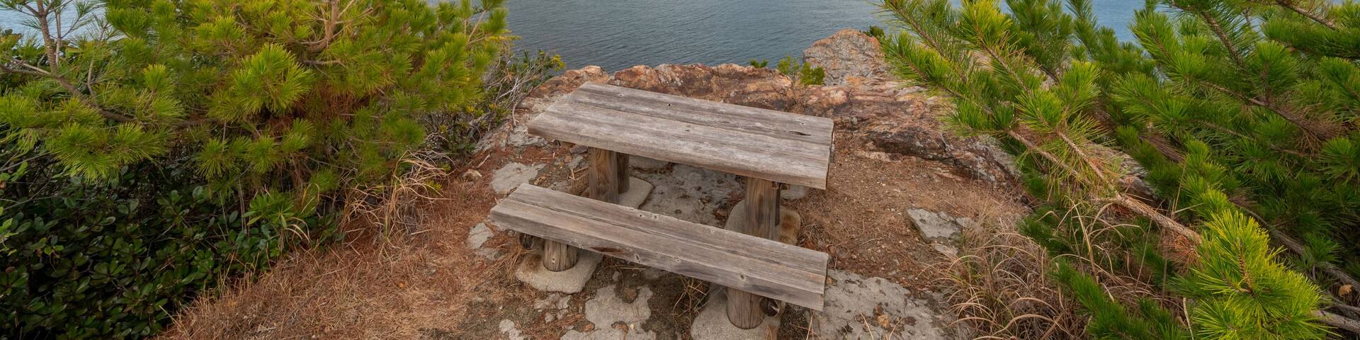 A wooden bench overlooking a calm lake with mountains in the background.