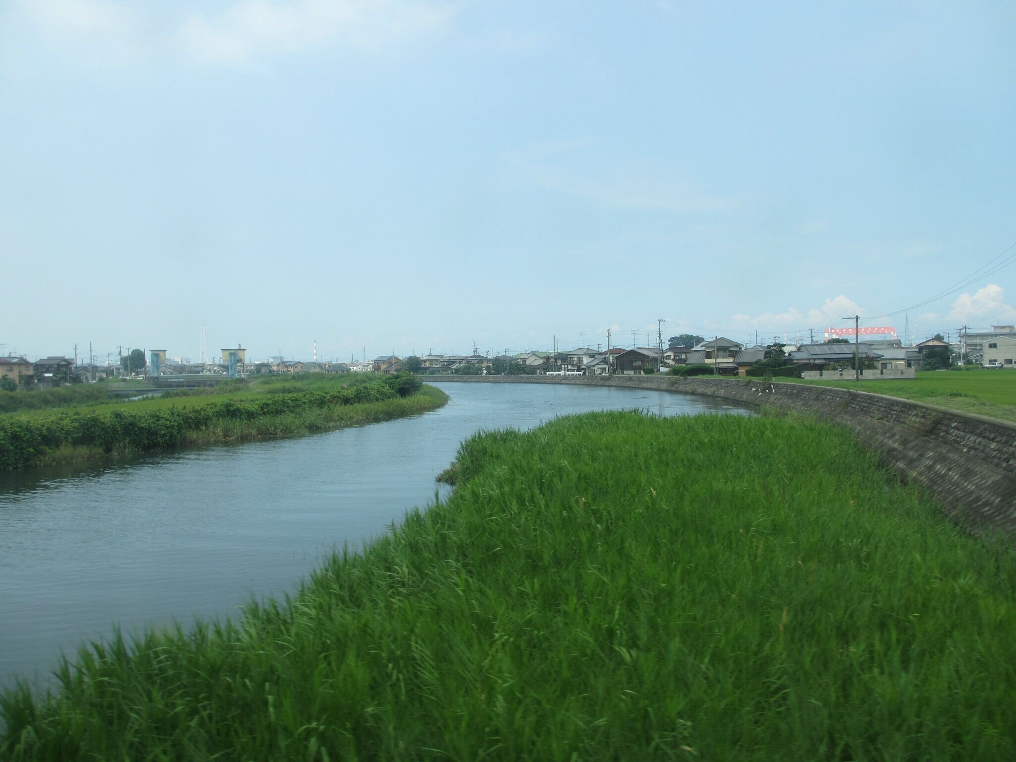 A river meandering through a rural area with houses and industrial structures in the background.