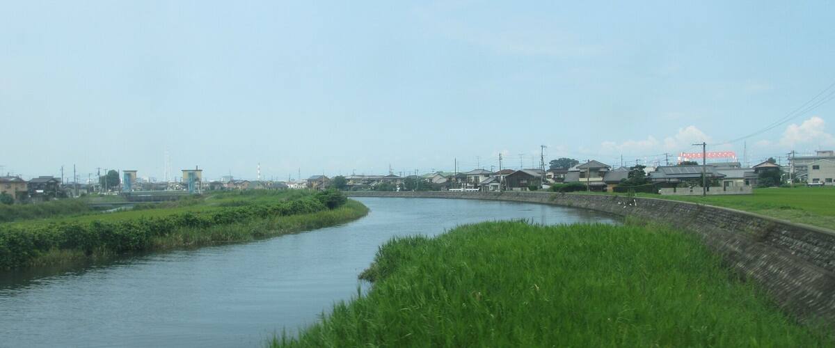 A river meandering through a rural area with houses and industrial structures in the background.
