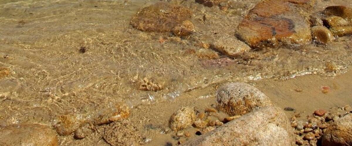 A clear lake with visible rocks and mountains in the background.