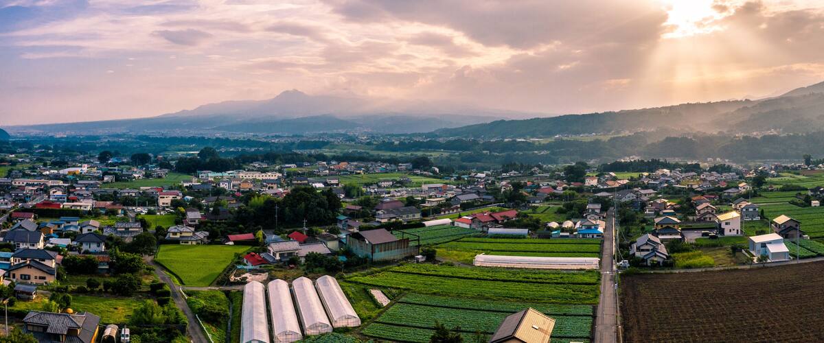A rural landscape with fields, houses, and mountains in the background.