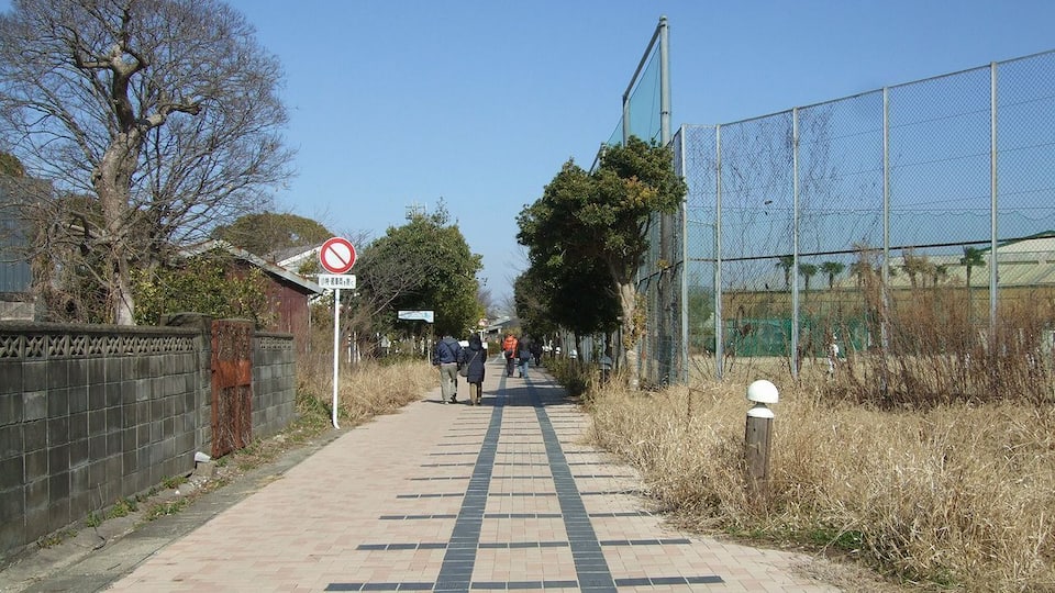 A paved walkway with a no-entry sign, a fence, and people walking.