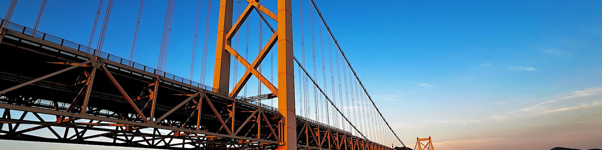 Uma grande ponte suspensa com várias faixas, atravessando um corpo d'água com um horizonte urbano ao fundo.