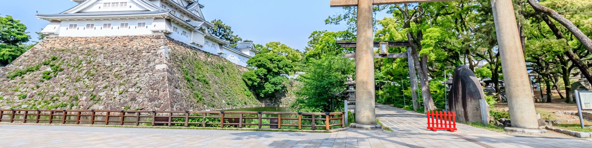 A traditional Japanese castle with a stone rampart and a torii gate in the foreground.