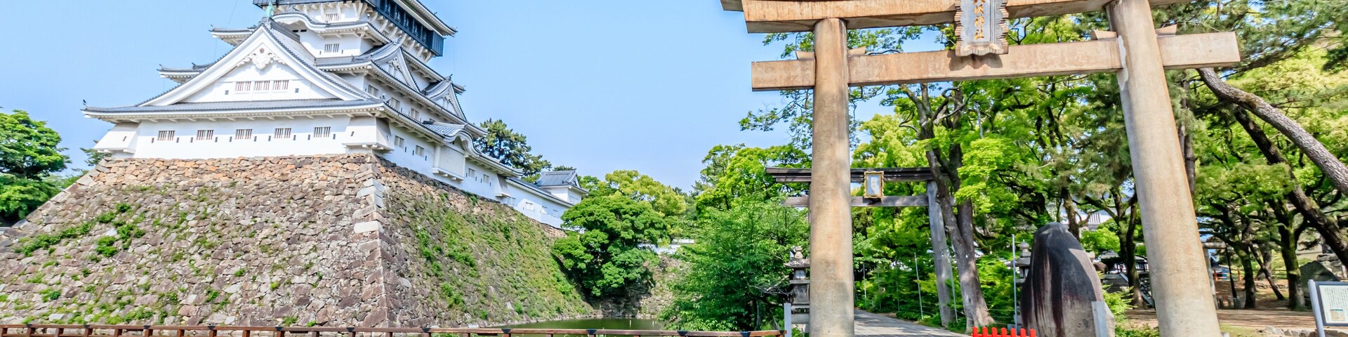 Um castelo japonês tradicional com uma muralha de pedra e um portão torii em primeiro plano.