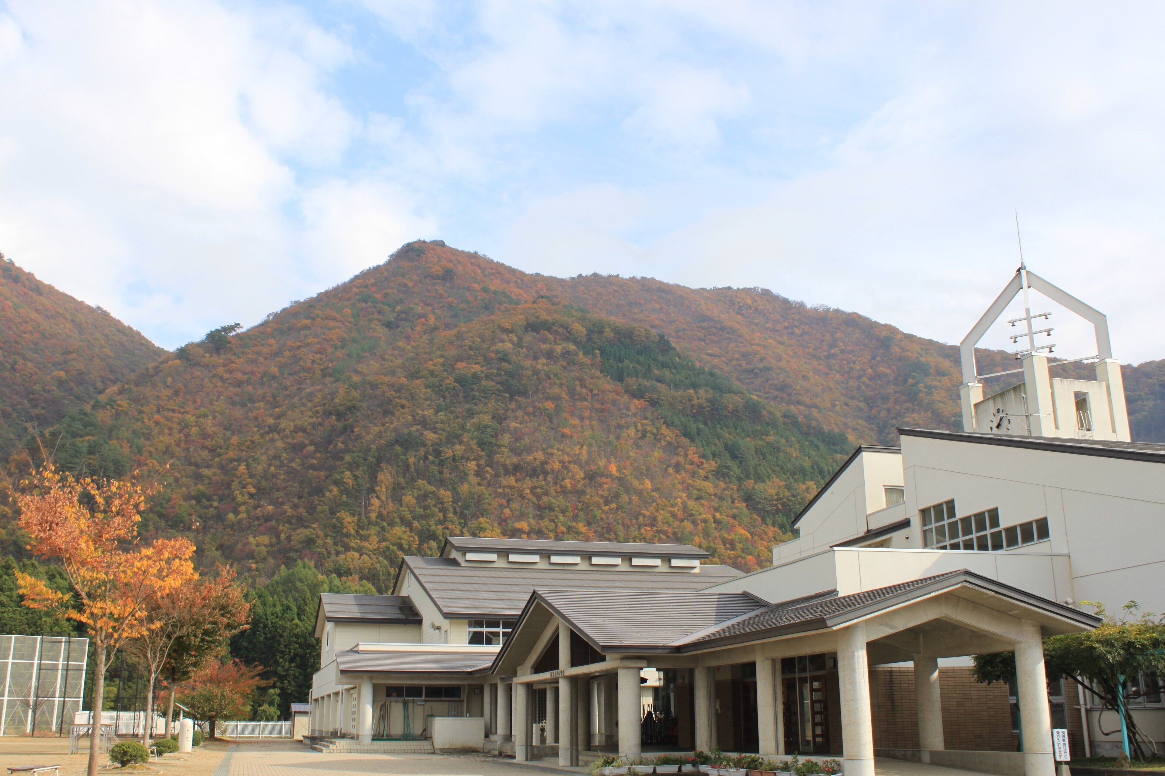 A modern building with a bell tower, surrounded by autumn-colored trees and a mountain in the background.