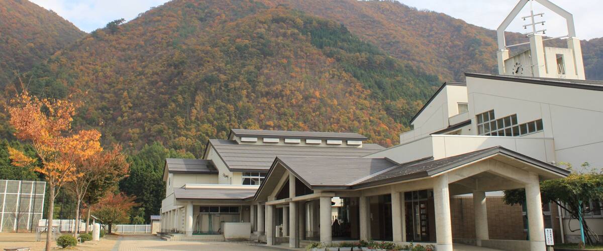 A modern building with a bell tower, surrounded by autumn-colored trees and a mountain in the background.
