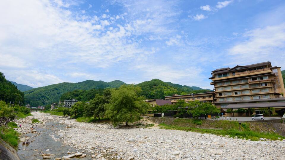 A river with rocks, a tree, and buildings in a mountainous area.