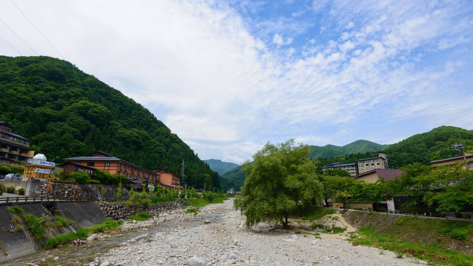 A river flowing through a valley with buildings on the banks, surrounded by lush green hills.