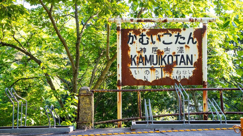 A weathered sign with Japanese characters and the word "KAMIKOTAN" in English, surrounded by lush greenery.