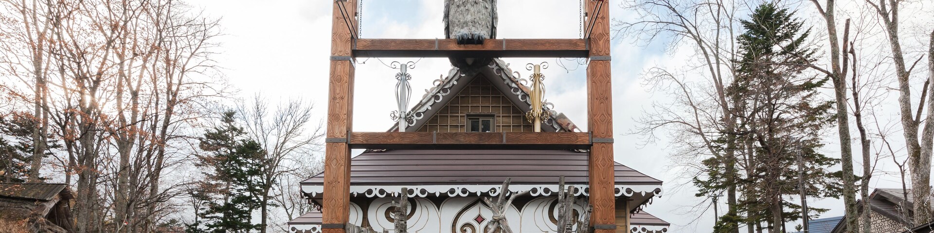 Um portão tradicional japonês com uma escultura de coruja, rodeado por árvores e um caminho de tijolos.