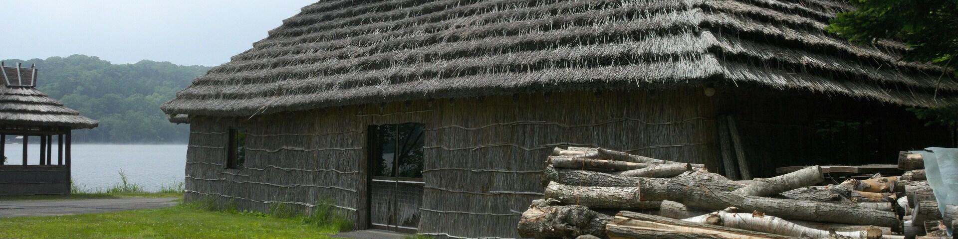 Una casa tradicional con techo de paja y estructura de madera, con un montón de leña en primer plano.