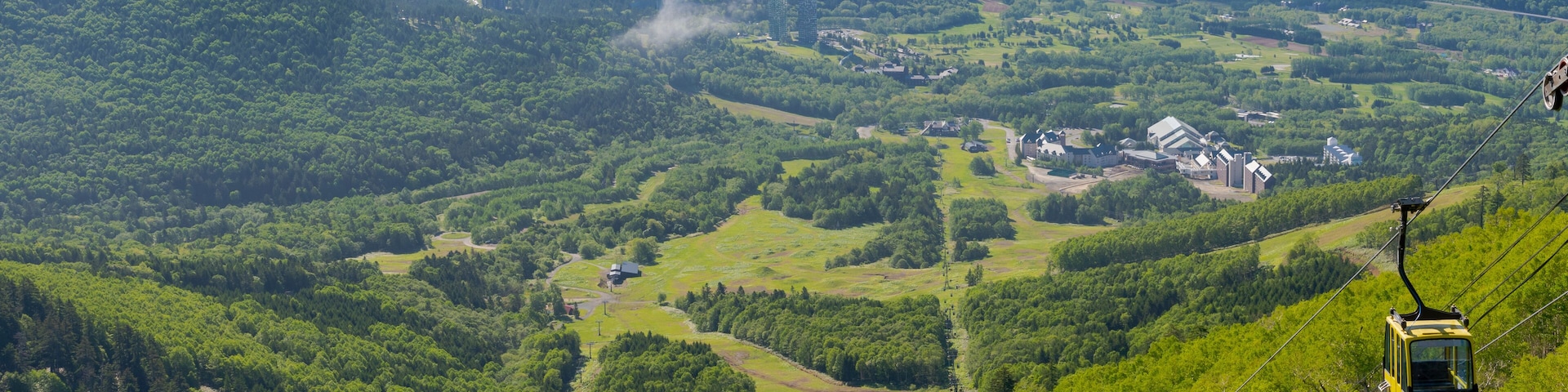 Um teleférico em um vale verdejante com edifícios e uma estrada sinuosa.