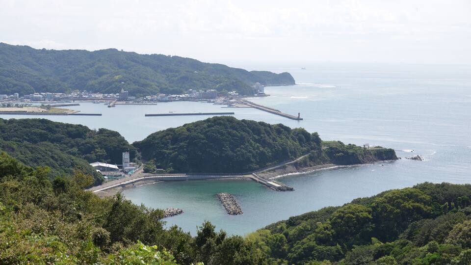 A coastal landscape with a bay, a pier, and a lighthouse.