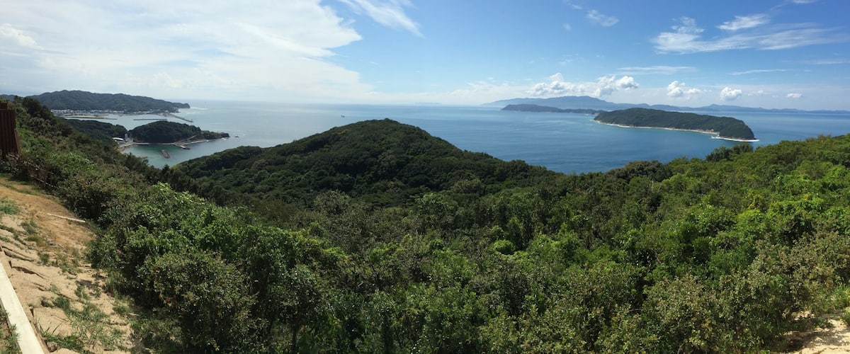 A coastal landscape with dense green hills, a clear blue sea, and distant islands.