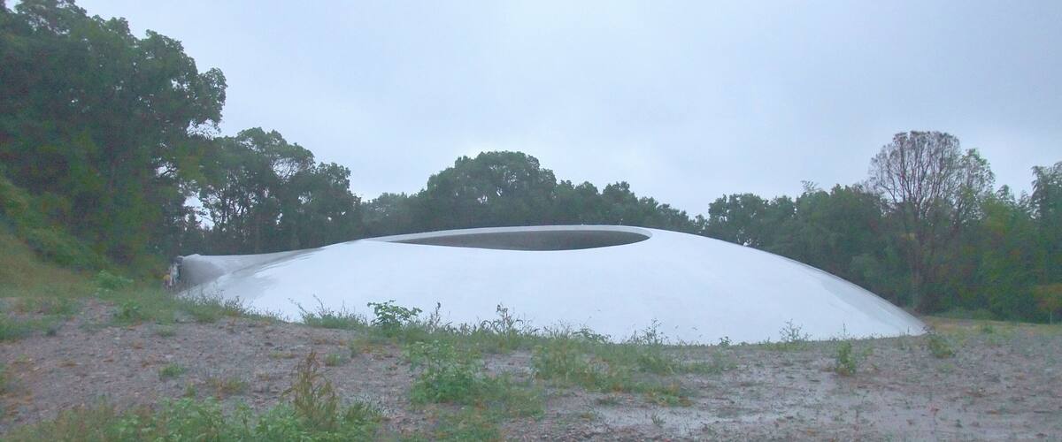 A large white dome structure in a natural setting with trees and a gravel path.