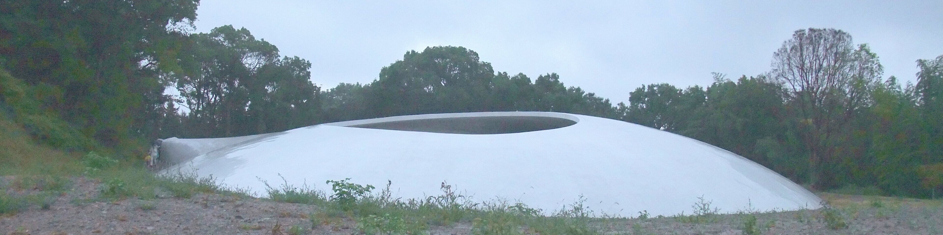 A large white dome structure in a natural setting with trees and a gravel path.