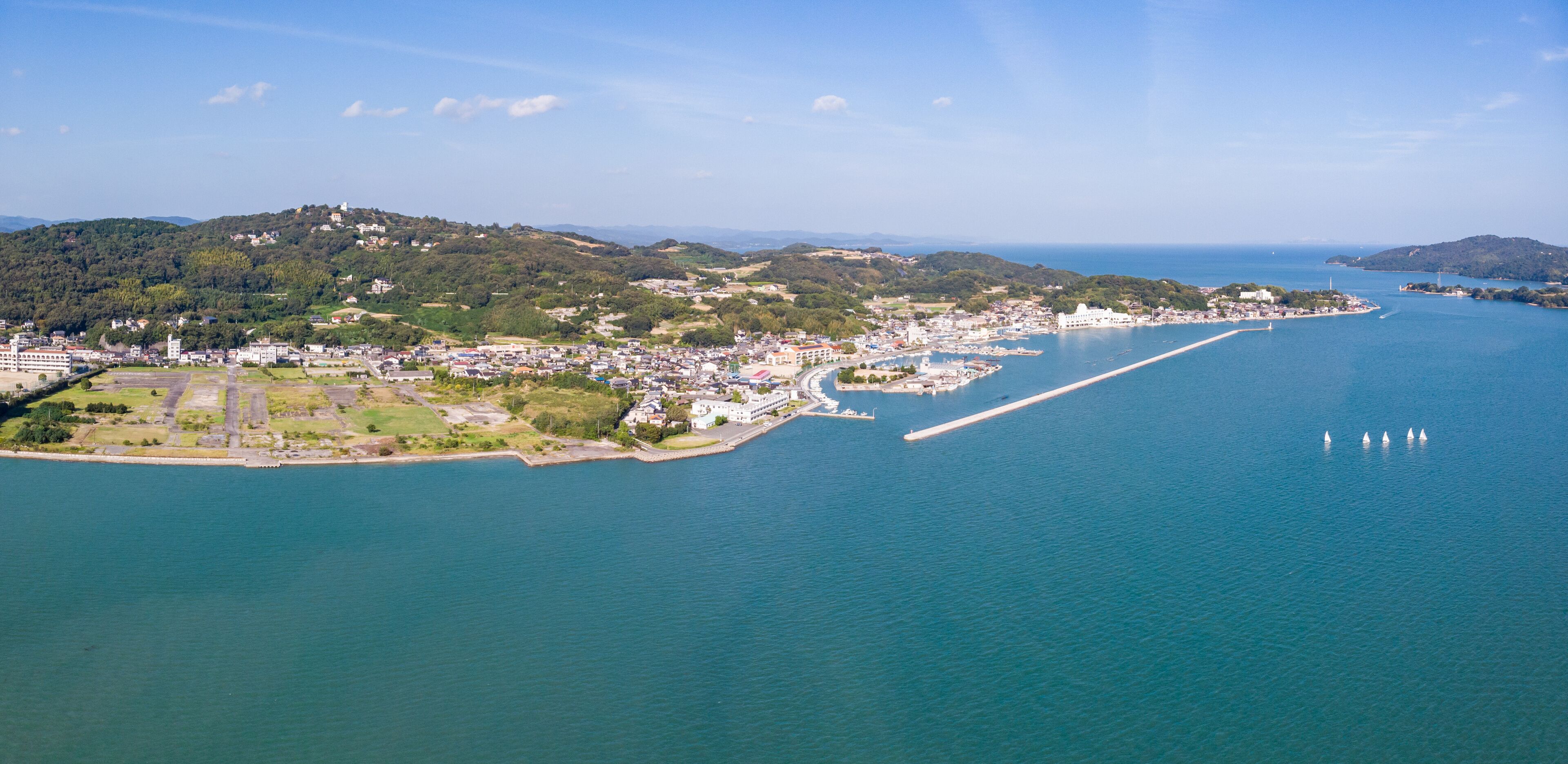 A coastal city with a marina, a large body of water, and hilly terrain in the background.