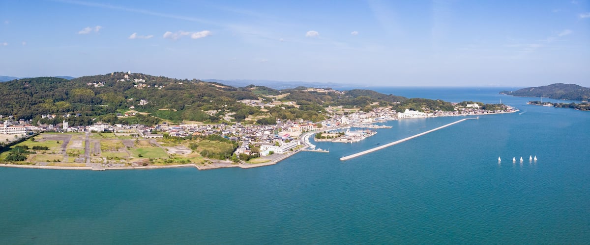A coastal city with a marina, a large body of water, and hilly terrain in the background.