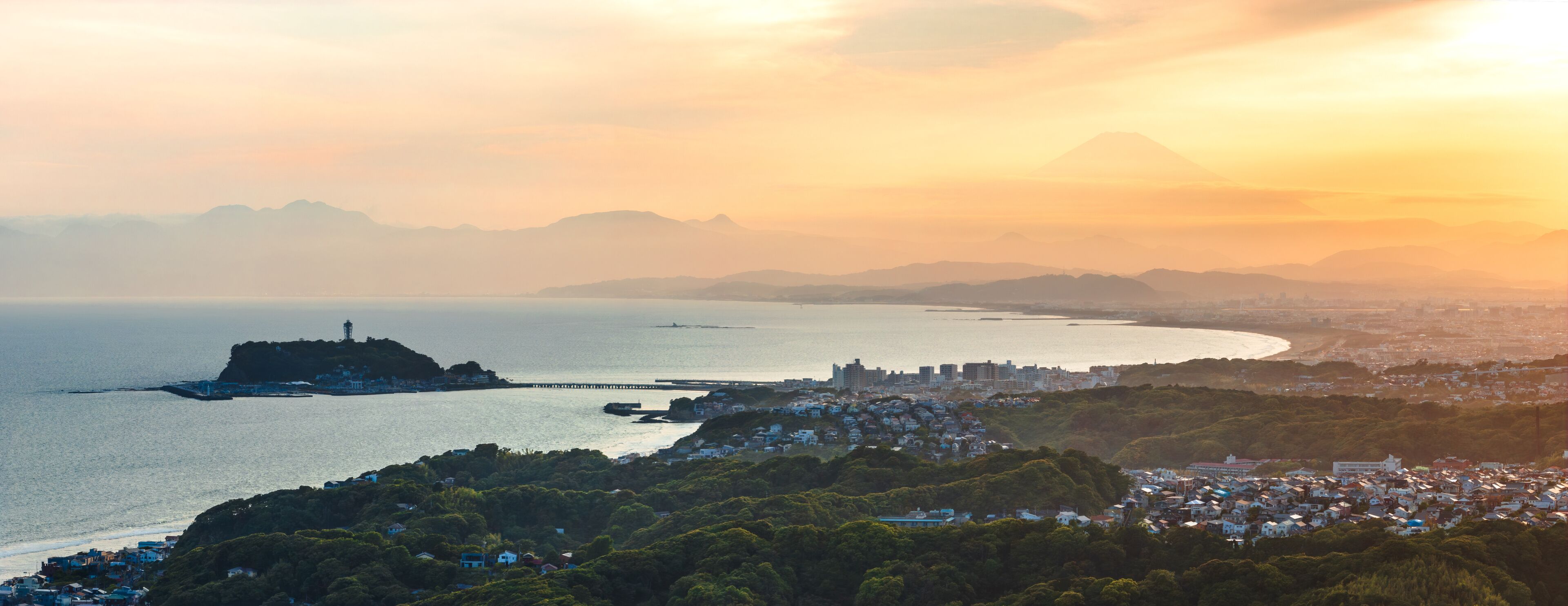 Aerial view of Enoshima Island and Mount Fuji shrouded in the distance under a golden sky, Kamakura, Kanagawa, Japan.
