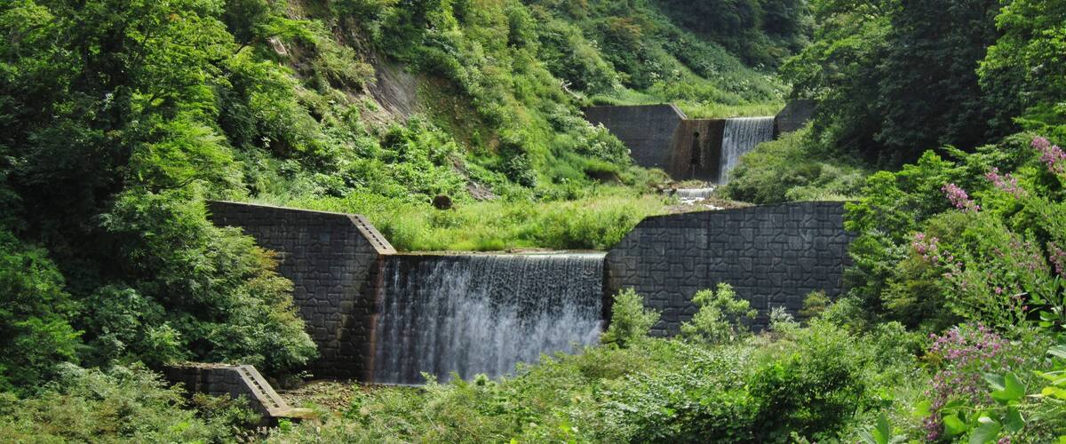 A waterfall cascading over a stone dam surrounded by lush greenery.