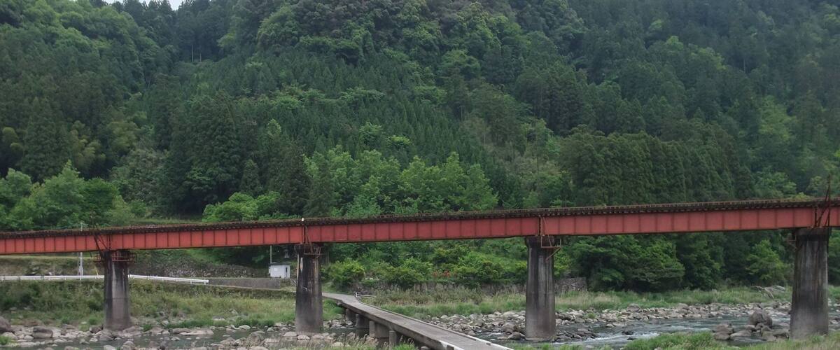 A red bridge over a river with a forested hillside in the background.