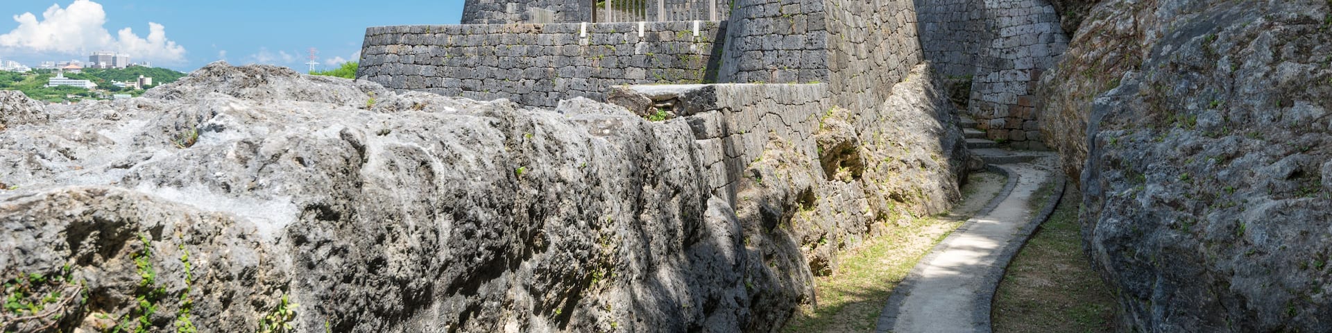 A stone fortification with a pathway leading up to it, surrounded by rocky terrain and greenery.