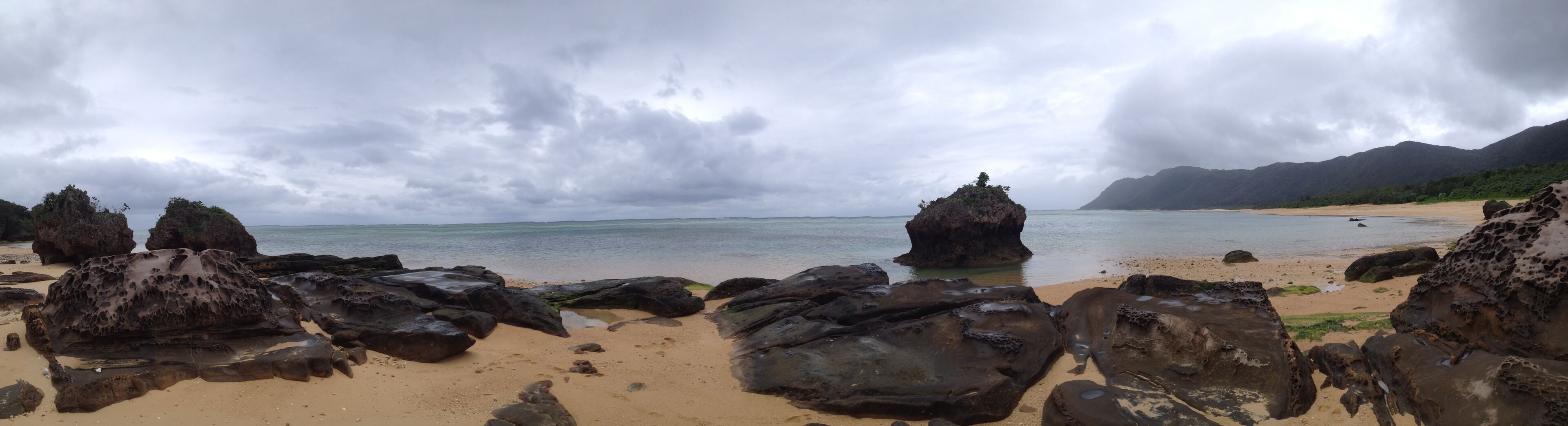 A beach with large rocks and a mountain in the background.
