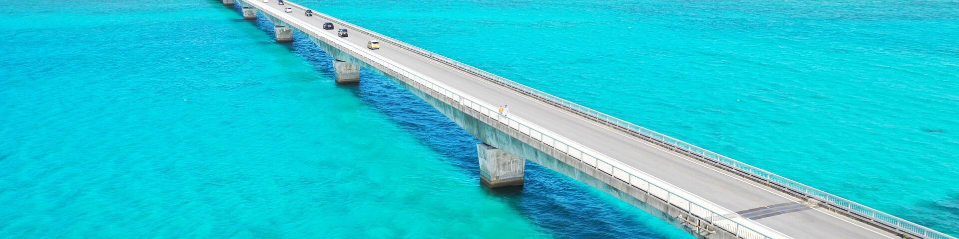 A long bridge over turquoise waters with a coastal town and a mountain in the background.