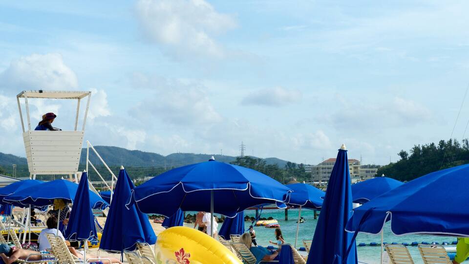 A beach with blue umbrellas, lounge chairs, and a lifeguard tower.