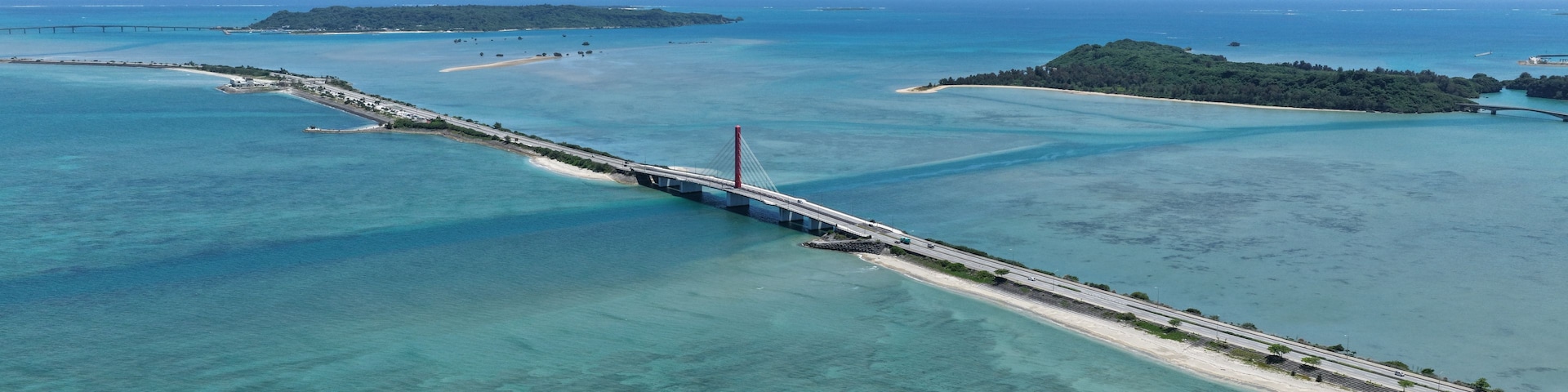 A bridge spanning a body of water with clear turquoise water and a sandy beach.